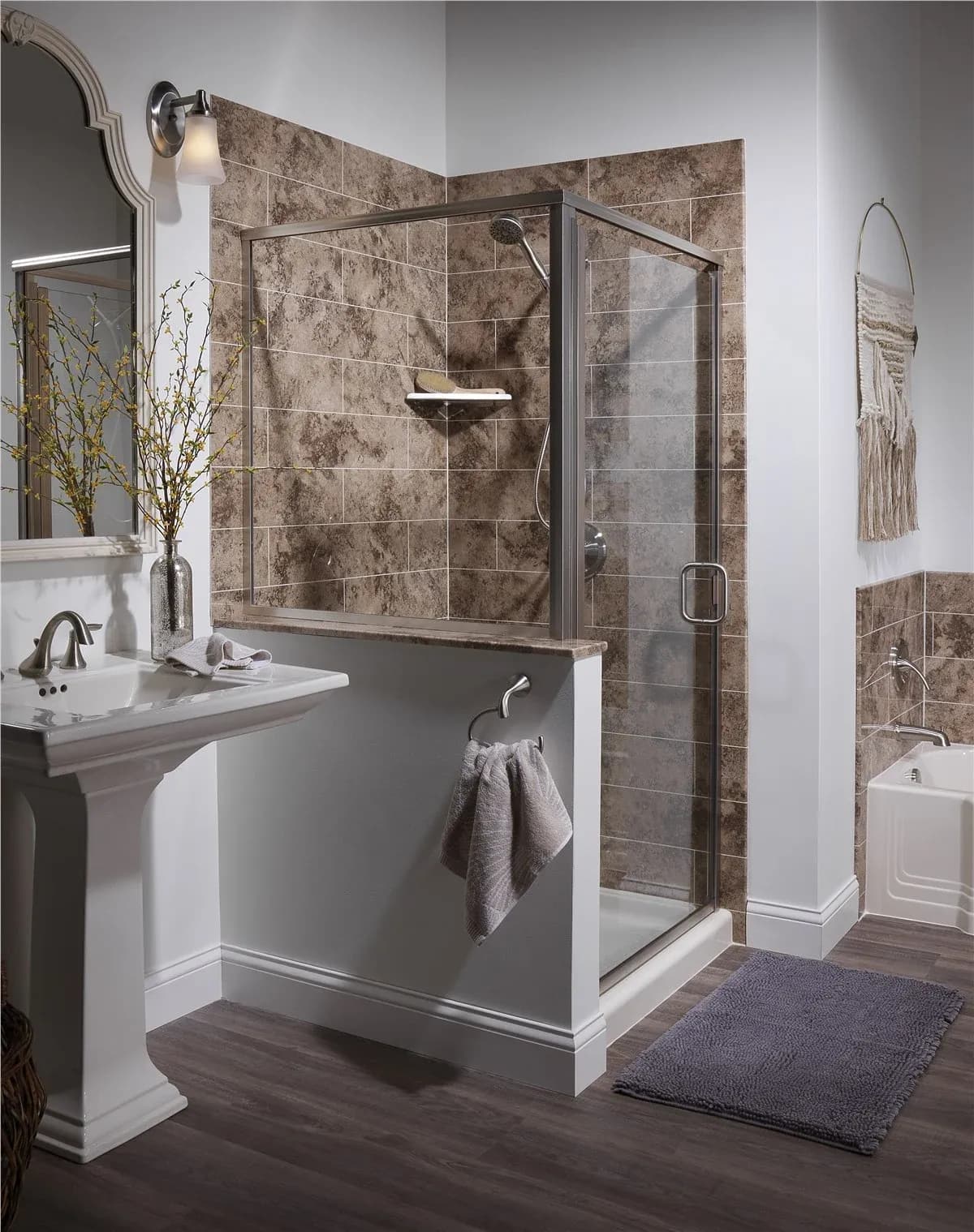 Modern bathroom with pedestal sink, framed mirror, wall sconce, and glass-enclosed shower with brown tile surround