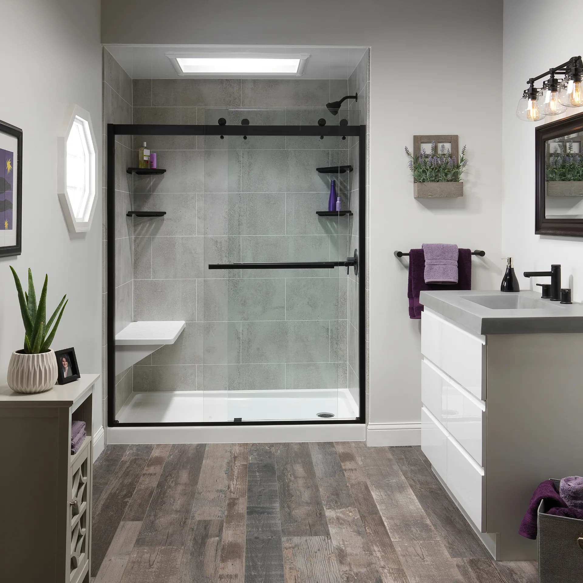 Modern bathroom with a large gray tiled walk-in shower, black-framed glass door, white vanity, and wood-look flooring.